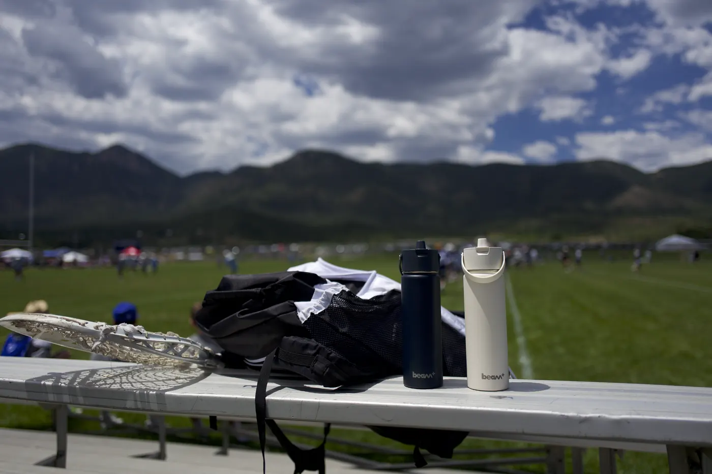 Two insulated bottles on a bleacher beside a sports field